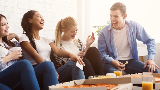 Estudiantes felices comiendo pizza y riendo en casa