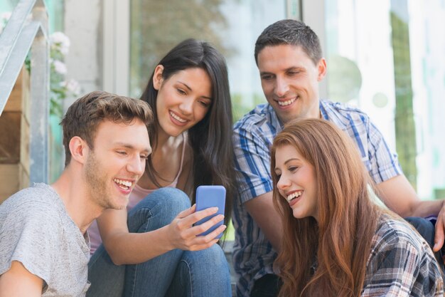 Foto estudiantes felices mirando el teléfono inteligente fuera del campus