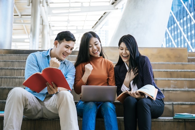 Estudiantes del grupo que estudian la investigación en la computadora portátil juntos que se sientan en la universidad.