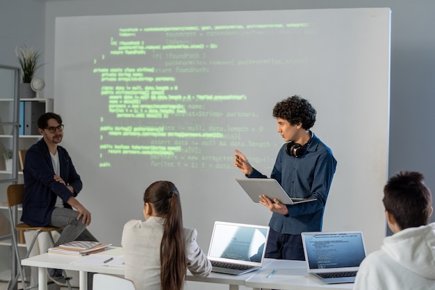 Uno de los estudiantes inteligentes con una computadora portátil de pie junto a la placa en el seminario y explicando los puntos principales de su presentación al maestro.