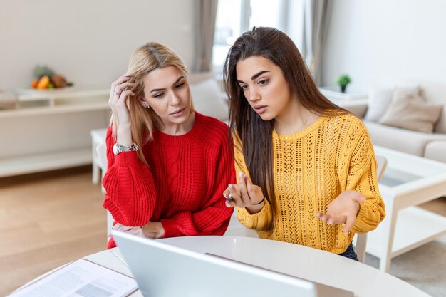 Estudiantes inteligentes discutiendo ideas para proyectos de cursos leyendo información de la red en computadoras portátiles mujeres jóvenes viendo tutorial juntas conversando en la oficina