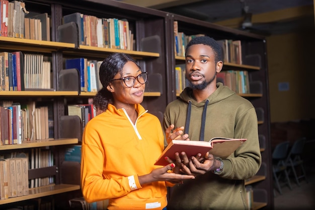 Estudiantes jovenes que sostienen un libro en una biblioteca