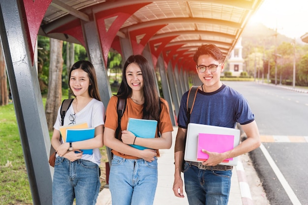 Estudiantes masculinos y femeninos se paran en libros y computadoras portátiles en el campus, concepto de educación