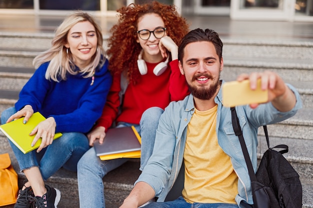 Estudiantes modernos en escaleras tomando selfie con teléfono móvil