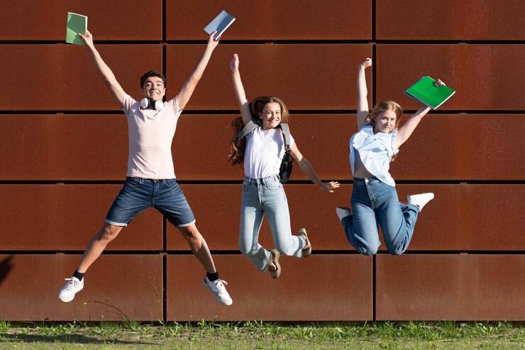 Estudiantes multiétnicos felices saltando y celebrando los buenos resultados en los exámenes y el final de las clases
