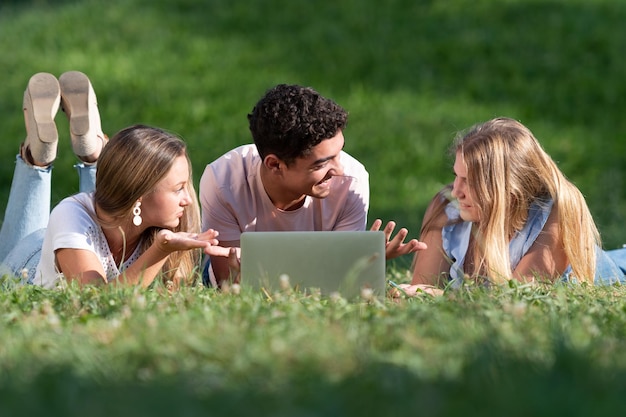 Estudiantes multiétnicos trabajando juntos en una laptop tirada en el césped