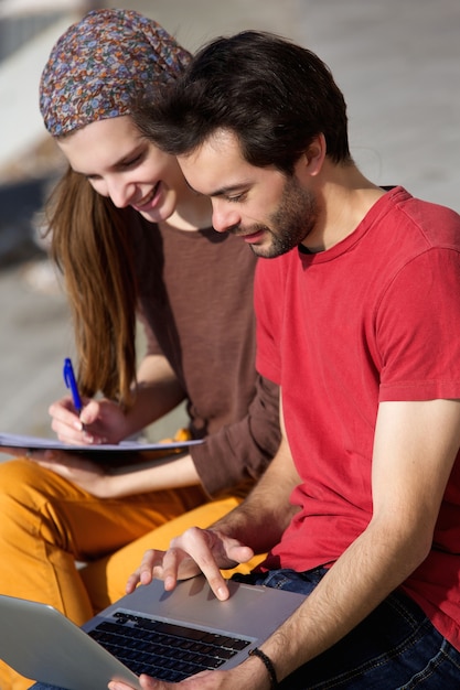 Estudiantes de la pareja trabajando juntos en la computadora portátil al aire libre