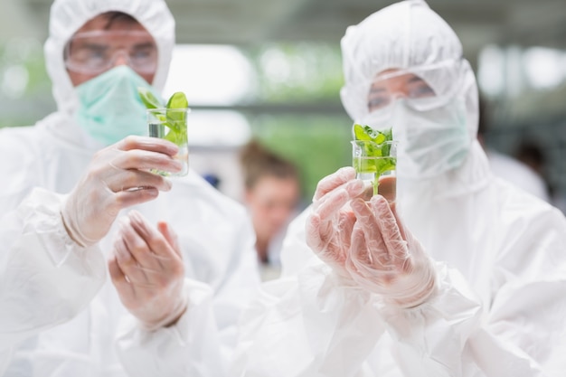 Estudiantes de pie en el laboratorio sosteniendo vasos con plantas