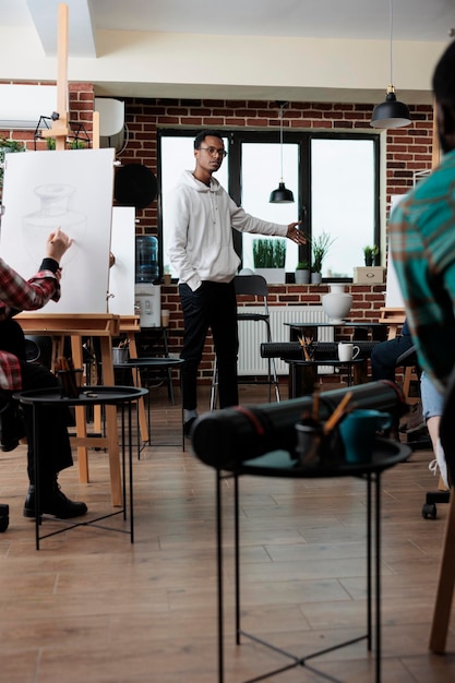 Foto estudiantes de pintura creando dibujos en lienzo usando lápiz gráfico durante un curso de arte en un estudio creativo. equipo multiétnico dibujando modelo de jarrón sobre lienzo trabajando en técnica creativa.