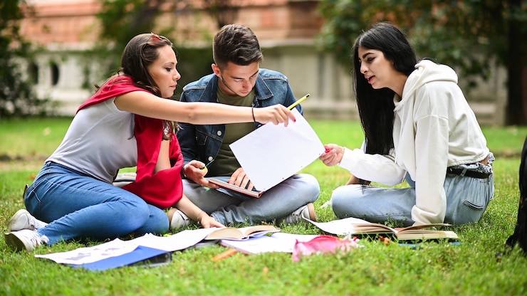 Foto estudiantes sentados en el césped y estudiando juntos en el parque.