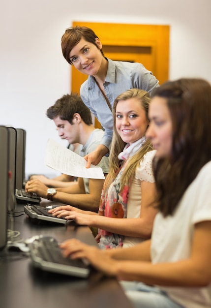 Estudiantes sentados en el maestro de la computadora sonriendo