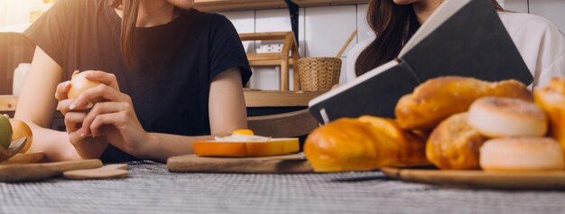 Estudiantes de sexo femenino anotando de los libros en la biblioteca de niñas asiáticas sentadas en el sofá usando computadora portátil y tableta para buscar información en línea en la sala de estar