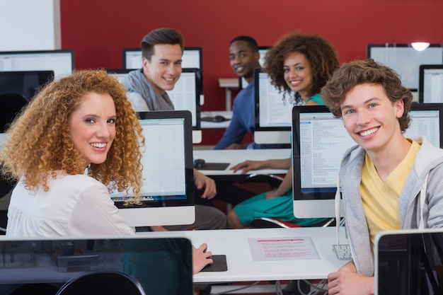 Estudiantes sonriendo a la cámara en clase de informática