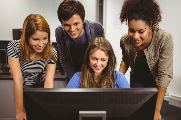 Estudiantes sonrientes que se sientan en el escritorio que usa la computadora junto