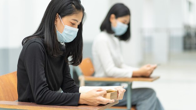 Estudiantes universitarias adolescentes que usan una máscara facial y mantienen la distancia mientras estudian en el aula y en el campus universitario para prevenir la pandemia de COVID-19. Educación foto de stock