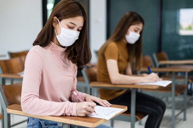 Las estudiantes universitarias adolescentes usan mascarilla y mantienen la distancia mientras estudian en el aula y en el campus universitario para prevenir la pandemia de COVID-19