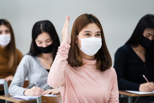 Las estudiantes universitarias adolescentes usan mascarilla y mantienen la distancia mientras estudian en el aula y en el campus universitario para prevenir la pandemia de COVID-19