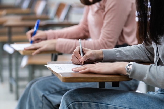 Las estudiantes universitarias jóvenes se concentran en hacer el examen en el aula. Las alumnas escriben seriamente el ejercicio de los exámenes en el aula.