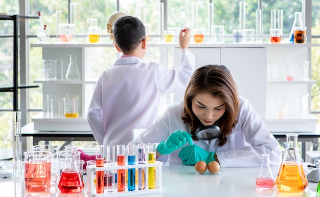 Estudiantes universitarios asiáticos concentrados que realizan experimentos con líquidos coloridos durante la investigación científica en el laboratorio.