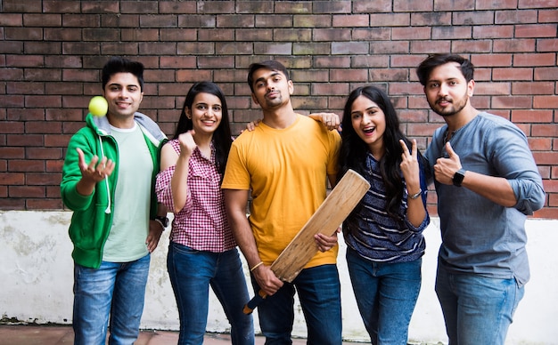 Estudiantes universitarios asiáticos indios o amigos jugando cricket match como actividad deportiva al aire libre