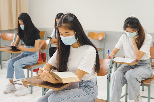 Los estudiantes universitarios asiáticos que regresan a la escuela usan mascarilla y mantienen la distancia estudiando en el aula