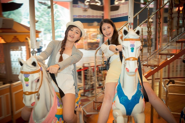 estudiantes universitarios asiáticos que van a hacer turismo en el extranjero jugando en el parque de atracciones local y montando un carrusel disfrutando alegremente de tomar una foto feliz juntos. color de película retro vintage.