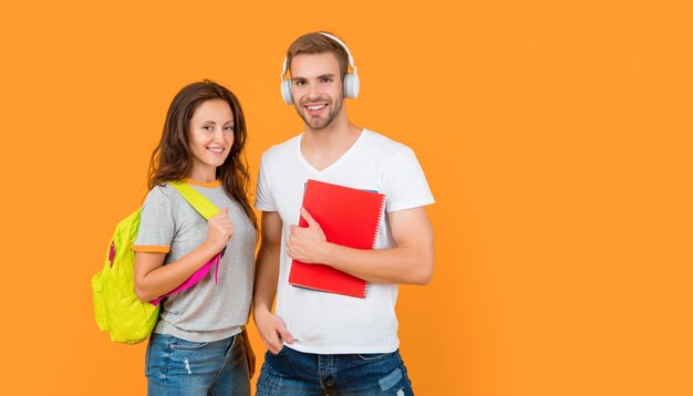 estudiantes universitarios felices en auriculares con libro de trabajo y mochila sobre fondo amarillo con educación de espacio de copia