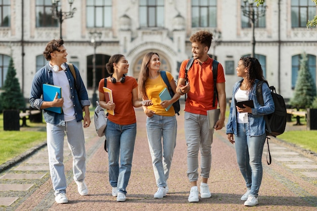 Estudiantes universitarios felices caminando juntos en el campus charlando y riendo