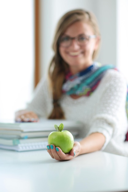 Estudiantes universitarios femeninos sentados en el escritorio con manzana en una pila de libros