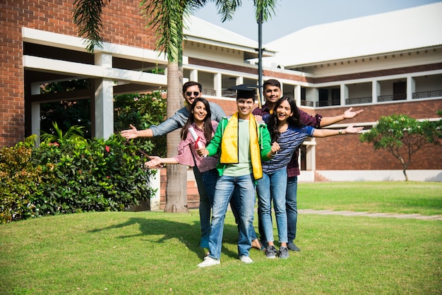 Estudiantes universitarios indios asiáticos reciben un certificado de grado mientras amigos celebran en el campus universitario al aire libre