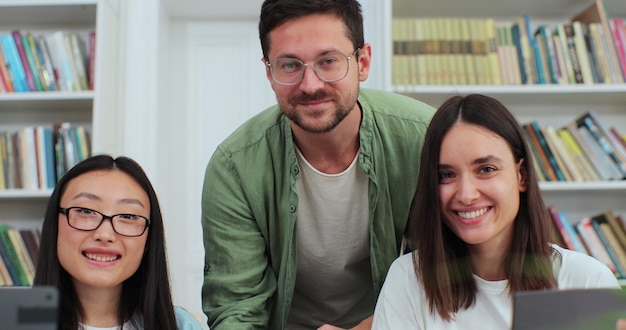 Foto estudiantes universitarios multiétnicos felices sonriendo mirando a la cámara posando en la biblioteca universitaria moderna concepto de tecnología moderna de estudio de educación