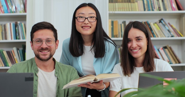 Estudiantes universitarios multiétnicos felices sonriendo mirando a la cámara posando en la biblioteca universitaria moderna Concepto de tecnología moderna de estudio de educación