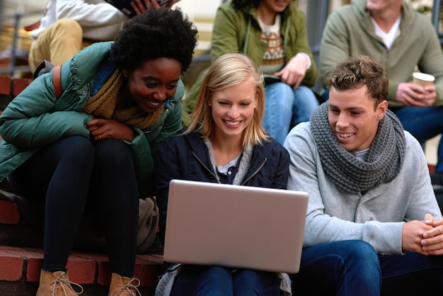 Foto estudiantes universitarios y portátiles en las escaleras al aire libre para la investigación relajarse o descansar en el campus con los medios sociales amigos universitarios o sonreír con la tecnología para la transmisión de internet o el aprendizaje y la diversidad