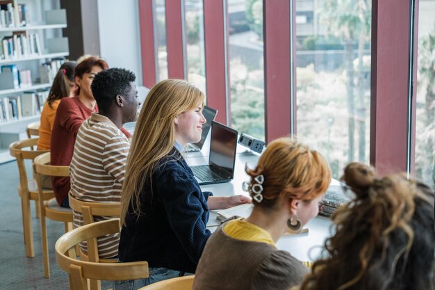 Estudiantes universitarios que estudian juntos en una biblioteca bien iluminada con una ventana grande