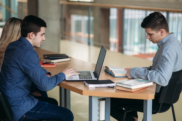 Estudiantes universitarios sentados juntos en la mesa con libros y una computadora portátil Jóvenes felices haciendo estudio grupal en la biblioteca