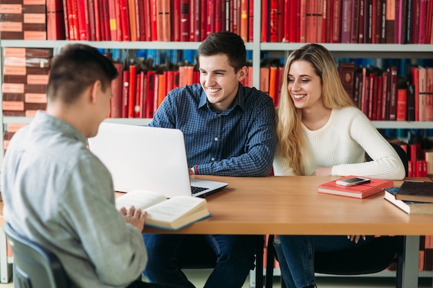 Foto estudiantes universitarios sentados juntos a la mesa con libros y portátil. jóvenes felices haciendo grupo