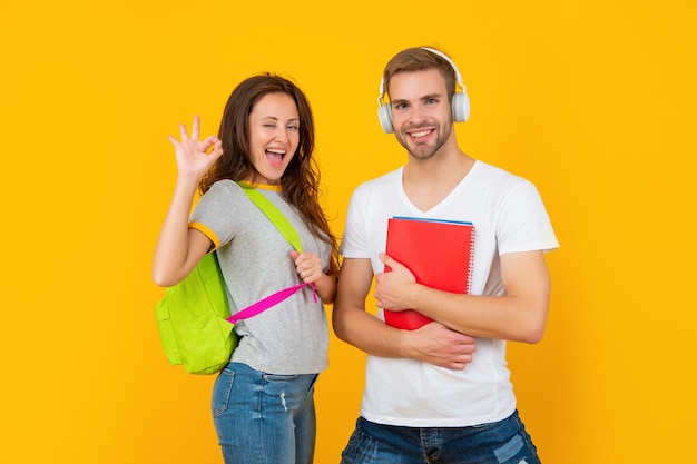 Estudiantes universitarios sobre fondo amarillo. estudiar con el libro de trabajo. está bien. feliz pareja en auriculares y mochila. De vuelta a la escuela. educación moderna. día del conocimiento. chico y chica sostienen cuaderno.