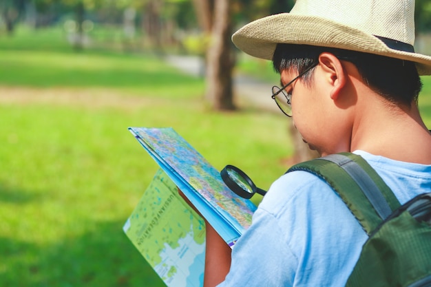 Estudiantes varones asiáticos llevando una mochila de viaje, con un sombrero, sosteniendo un mapa para viajar para aprender