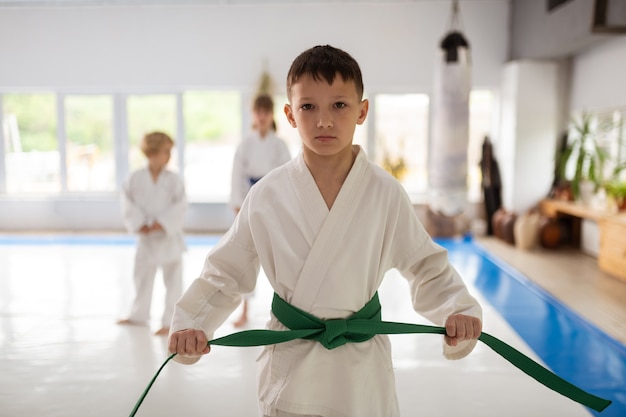 Estudiar artes marciales. Grave muchacho de pelo oscuro estudiando artes marciales vistiendo kimono y cinturón verde