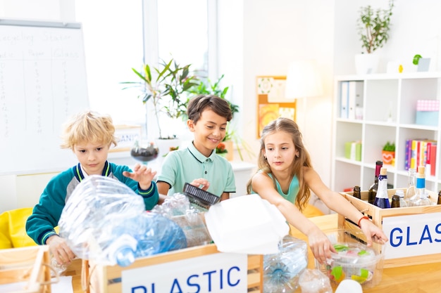 Estudiar la clasificación de residuos. Niños radiantes inteligentes que estudian la clasificación de residuos en la lección de ecología en la escuela