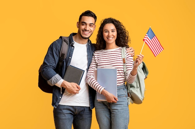 Estudiar en el extranjero sonriente pareja de estudiantes del Medio Oriente posando con bandera estadounidense