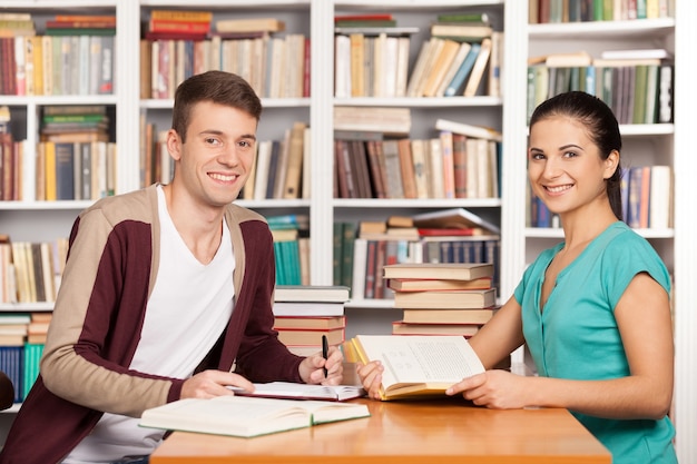 Estudiar juntos. Alegre joven y mujer sentada en el mostrador de la biblioteca y sonriendo