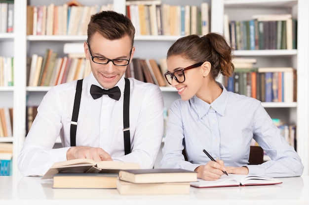 Estudiar juntos. Pareja joven alegre nerd en vasos preparándose para los exámenes mientras están sentados juntos en la biblioteca