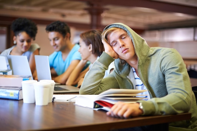 Estudiar lo aburre Un joven estudiante que parece aburrido mientras sus compañeros de clase estudian en segundo plano