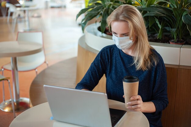 Estudiar y trabajar durante la epidemia. Distancia social. Una mujer rubia sentada en una mesa en un café vacío.