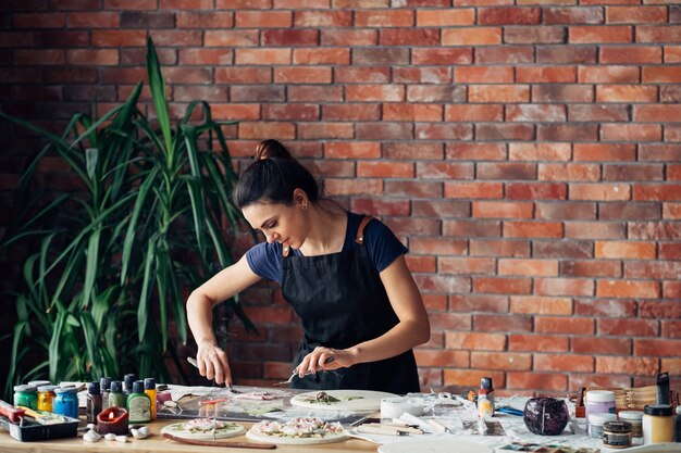 Estudio de artista. Artesanía de arcilla en proceso. Mujer joven con variedad de herramientas de modelado en el lugar de trabajo