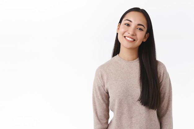 Foto estúdio de cintura sorrindo feliz e macia estudante universitária asiática com longos cabelos escuros inclinando a cabeça bonito e bobo sorrindo entusiasmado tendo uma deliciosa conversa despreocupada em pé alegre