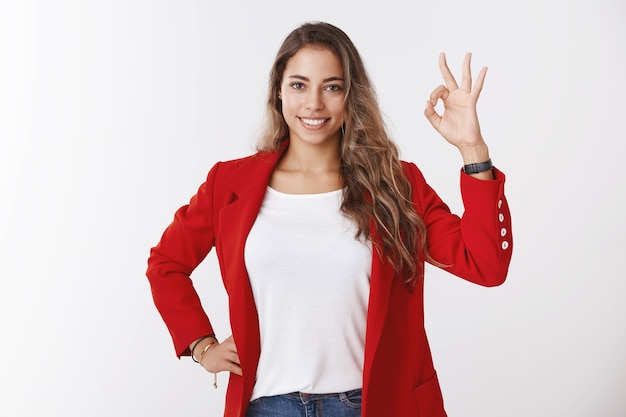 Estudio de disparo atractiva mujer de 25 años de pelo rizado jefe de equipo con chaqueta roja que aprueba la idea del gusto del proyecto que muestra un gesto satisfactorio aceptable sonriendo, encantado de trabajo en equipo perfecto