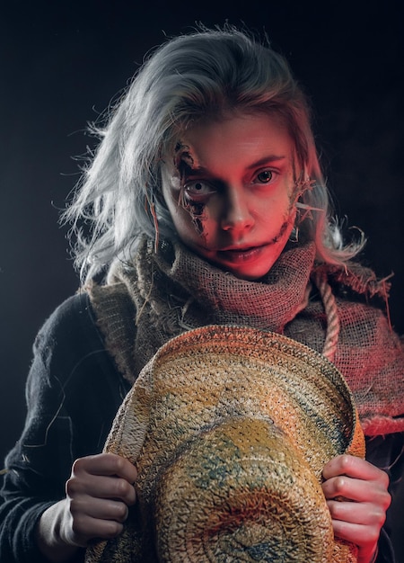 En el estudio fotográfico oscuro, una mujer bonita con un maquillaje espeluznante posa para el fotógrafo.