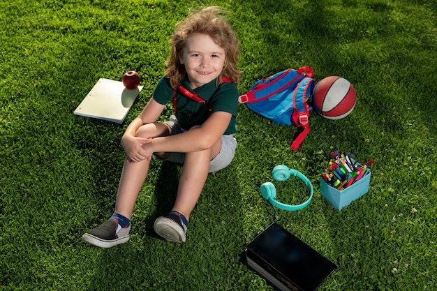 Estudio infantil en el parque de verano Niño lindo con útiles escolares sentado en el parque de la escuela primaria Educación temprana para niños pequeños Tarea al aire libre Estudiante de preescolar al aire libre